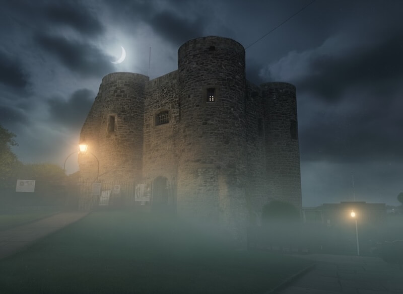 Ypres Tower (Rye Castle Museum) in fog at night with crescent moon and lamplight.
