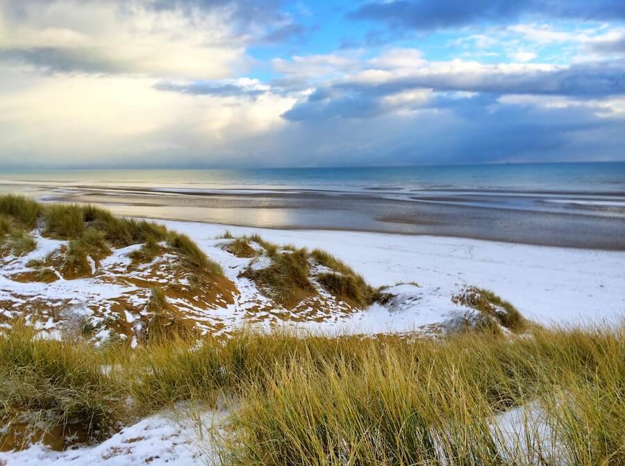 Winter walk along Camber Sands beach with a dramatic sky and waves crashing on the shore.