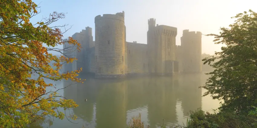 Bodiam Castle, its moat surrounded by mist and fiery autumn leaves