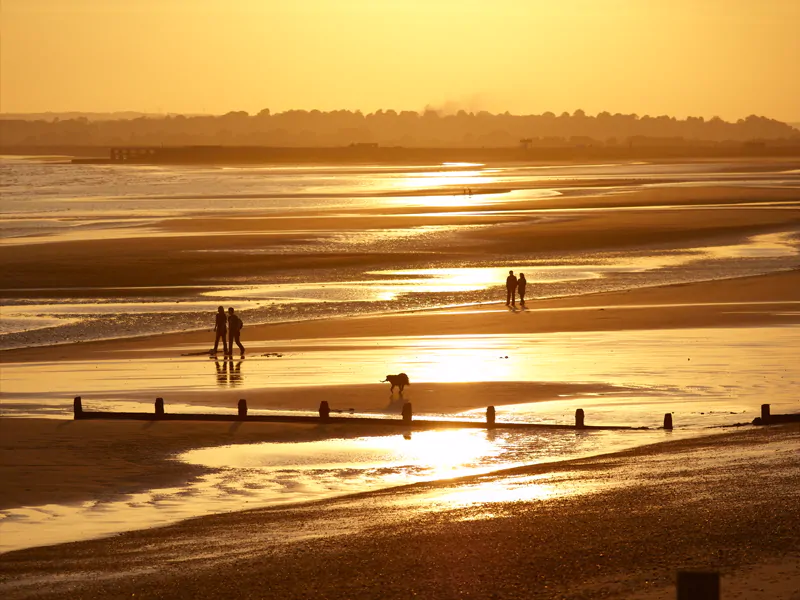 Camber Sands beach at sunset in autumn with golden light and calm waves.